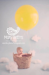Child in basket with helium-filled yellow balloon above him