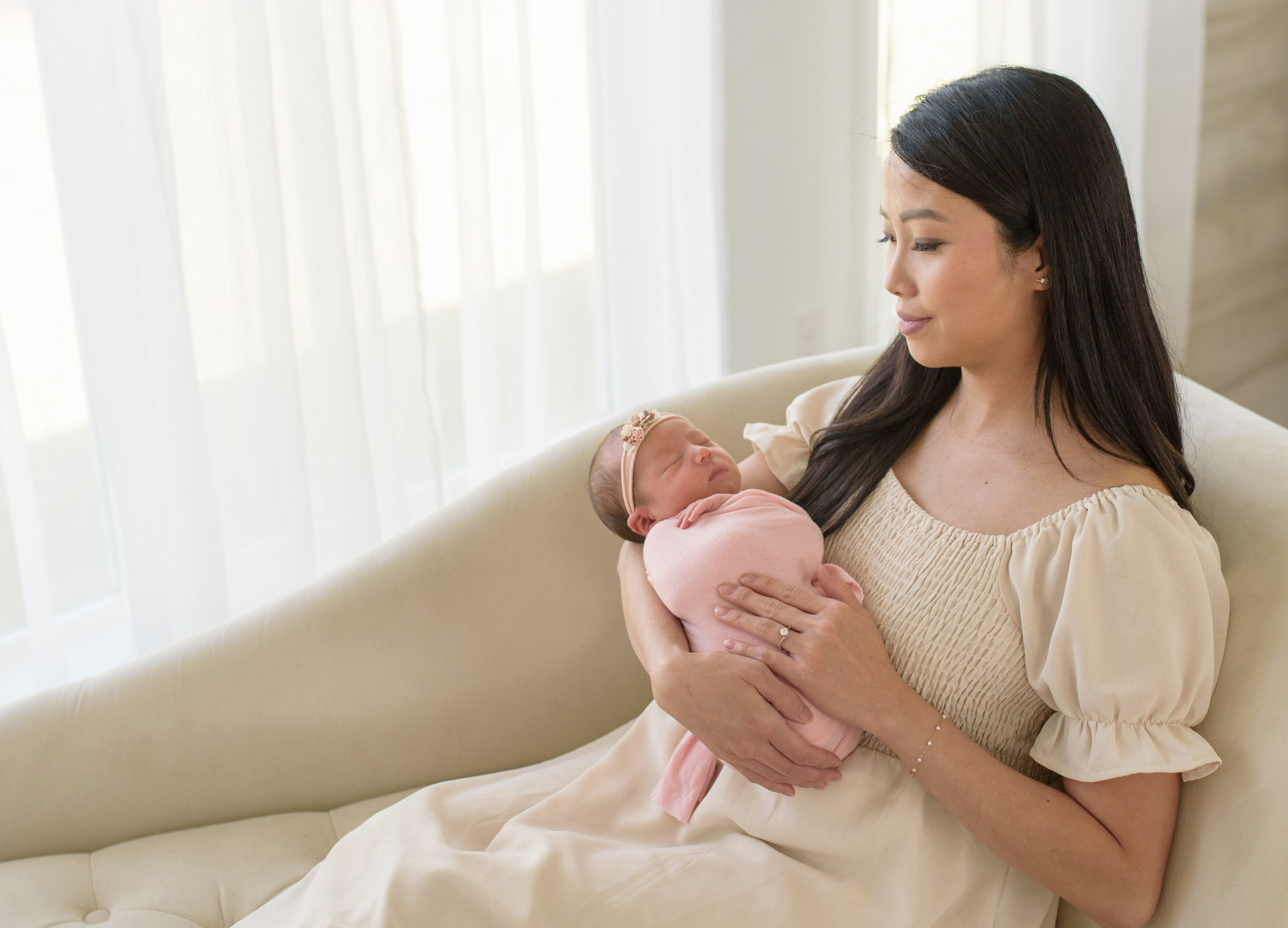 Mother and newborn baby girl in pink wrap in studio setting.